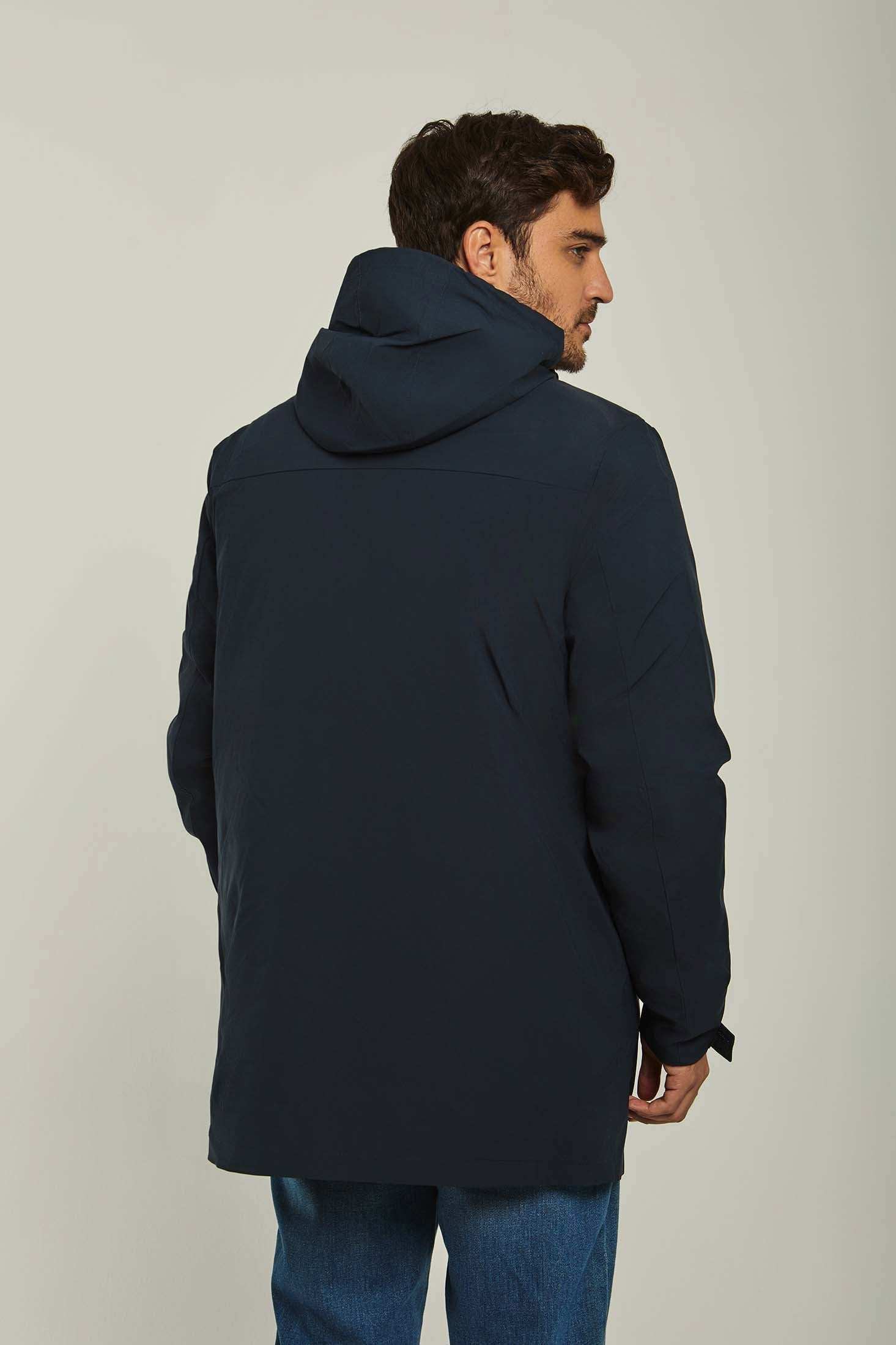 Man wearing dark blue hooded jacket and blue jeans, back view, against plain background