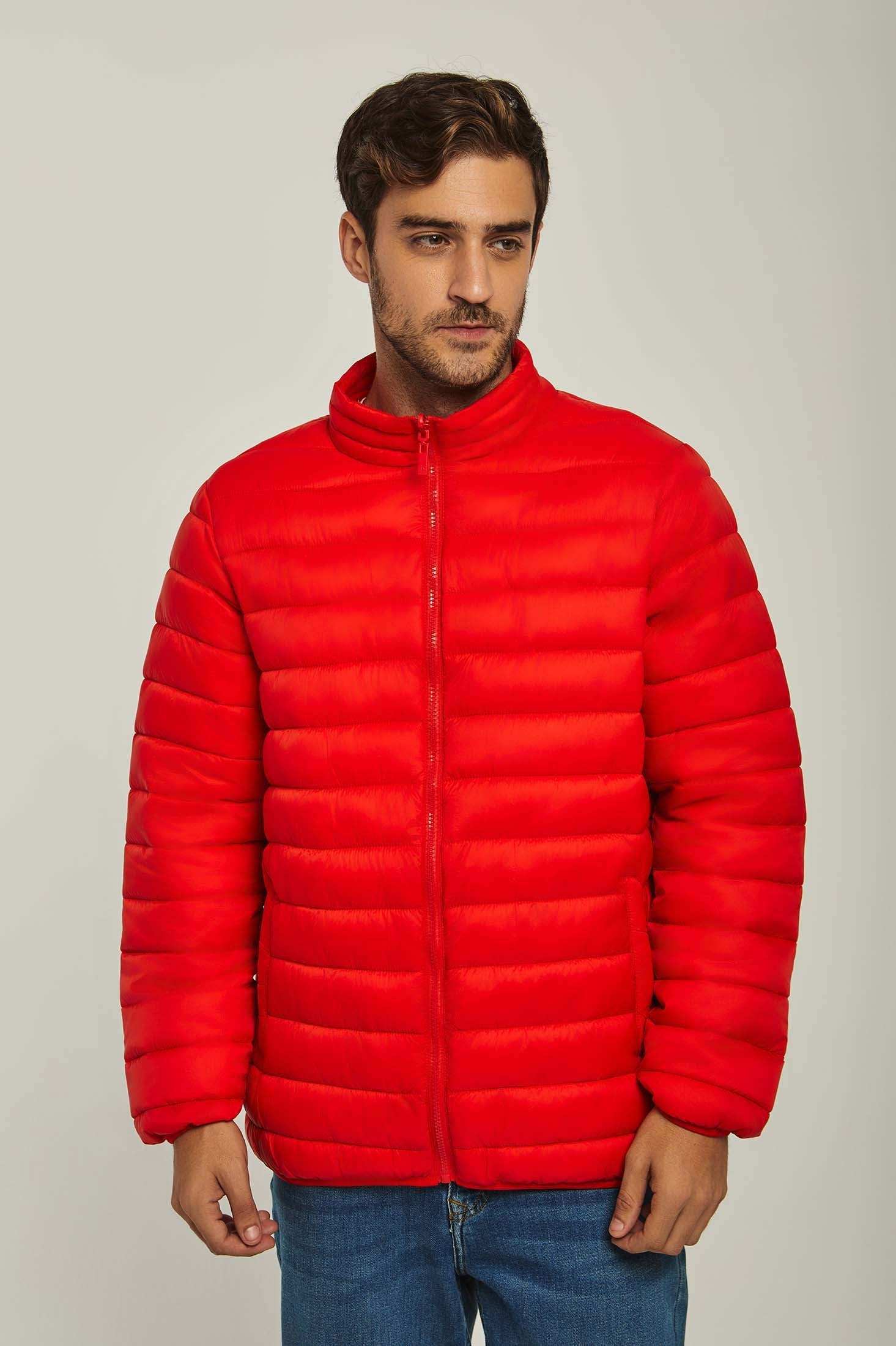 Man wearing a bright red puffer jacket with zip front and blue jeans on a neutral background