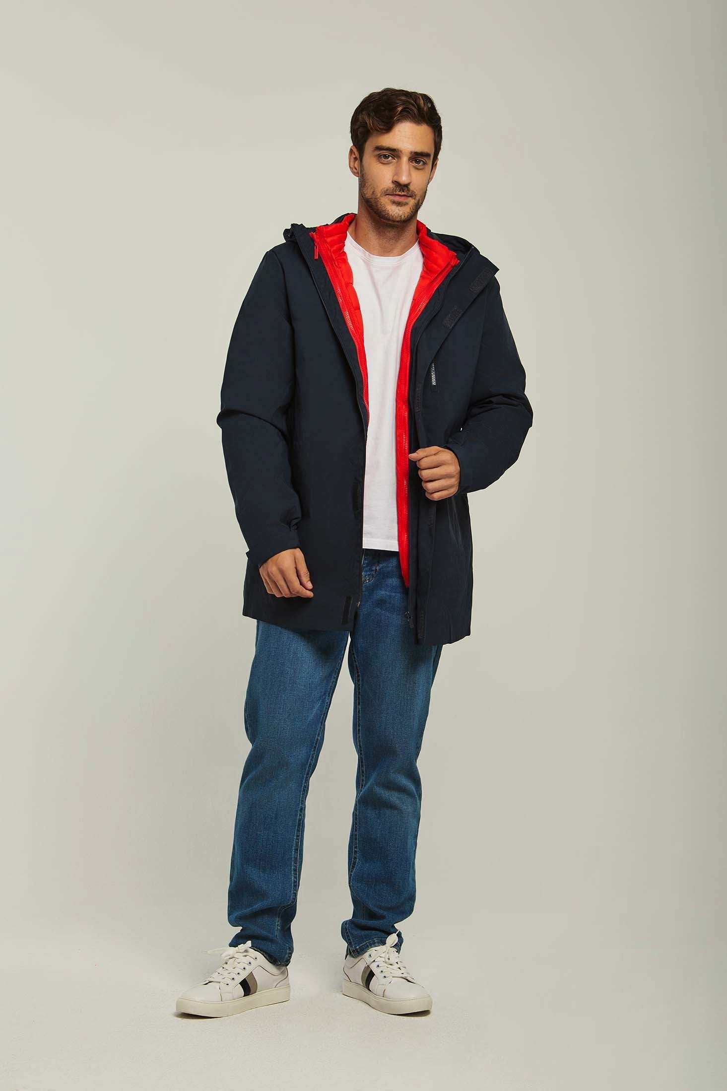 Man wearing a navy hooded jacket with red lining, white t-shirt, blue jeans, and sneakers