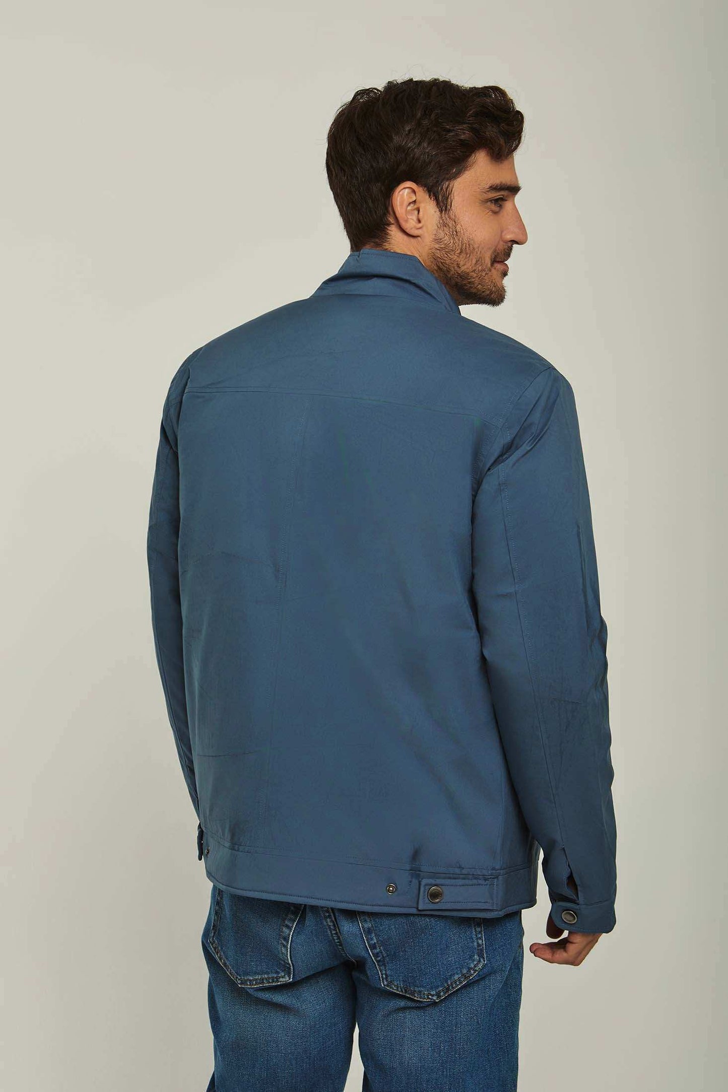 Man wearing a blue casual jacket and blue jeans, back view, neutral background