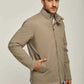 Man wearing a beige zip-up casual jacket with jeans on a plain light background