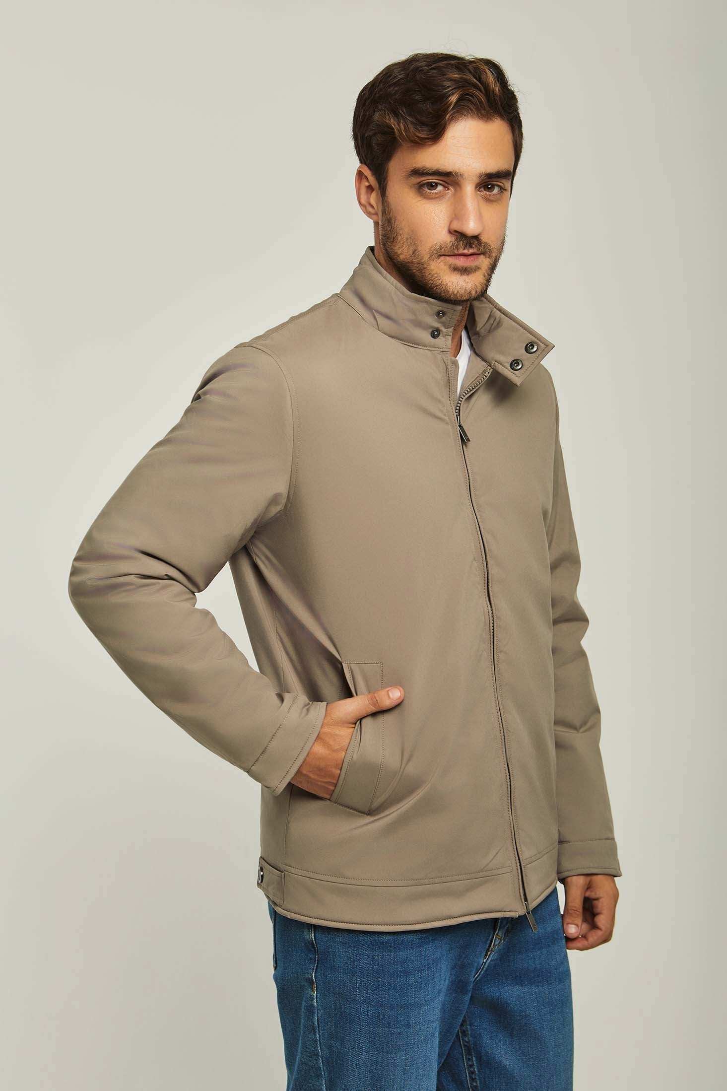 Man wearing a beige zip-up casual jacket with jeans on a plain light background