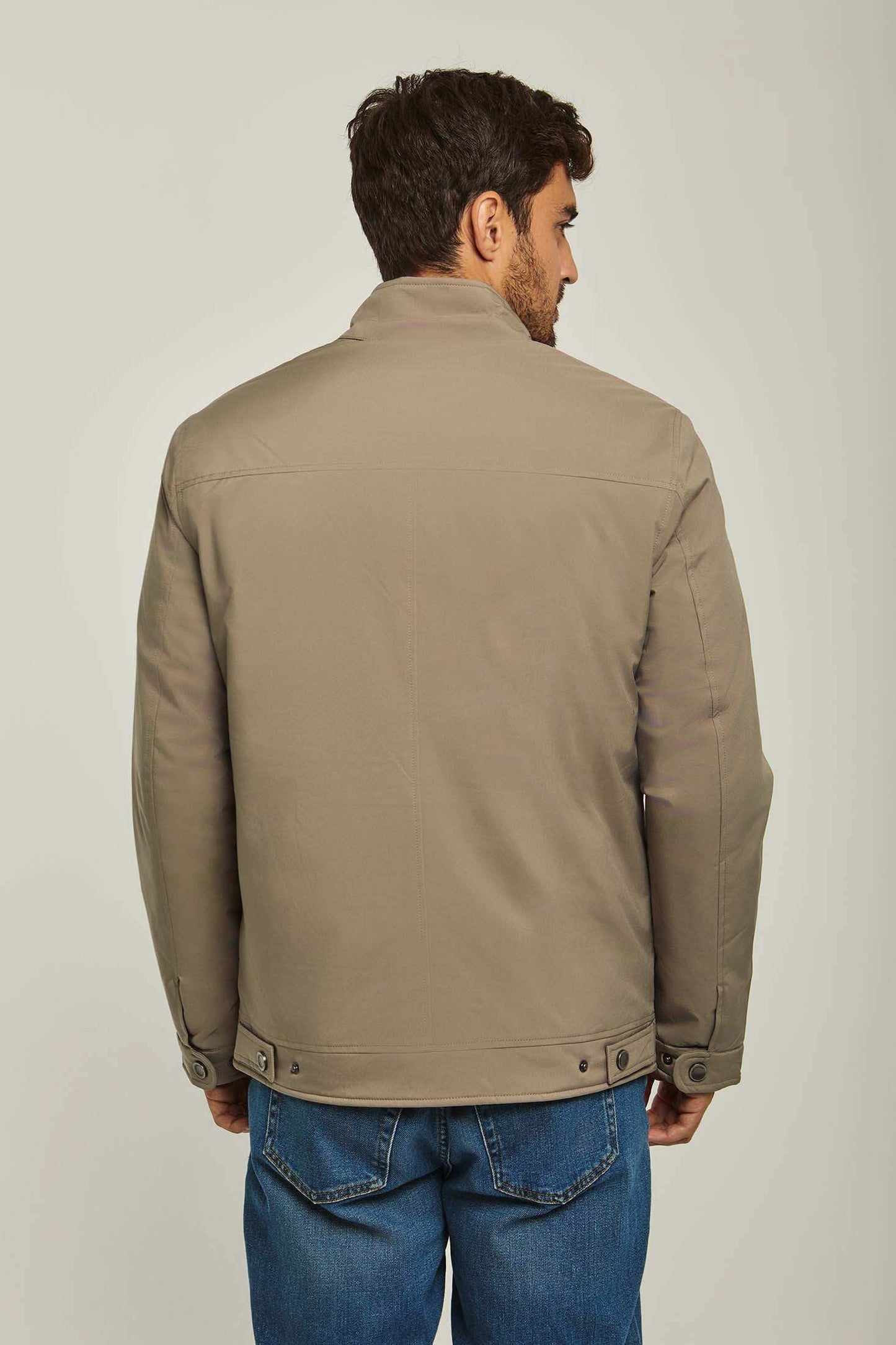 Man wearing beige casual jacket and blue jeans, back view on neutral background