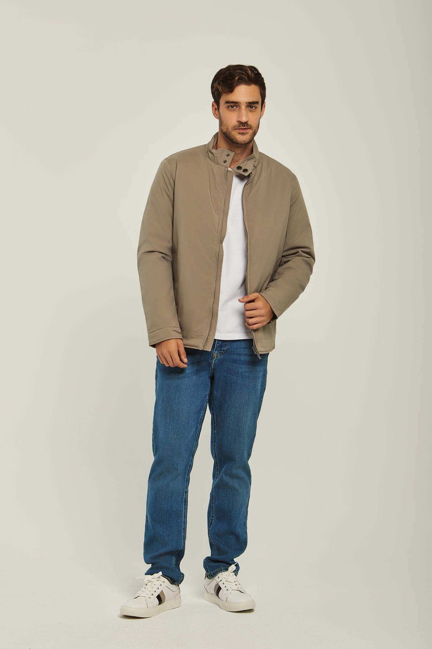 Man wearing a taupe casual jacket, white t-shirt, blue jeans, and white sneakers