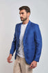 Man wearing a blue blazer, white t-shirt, and beige pants on a plain background