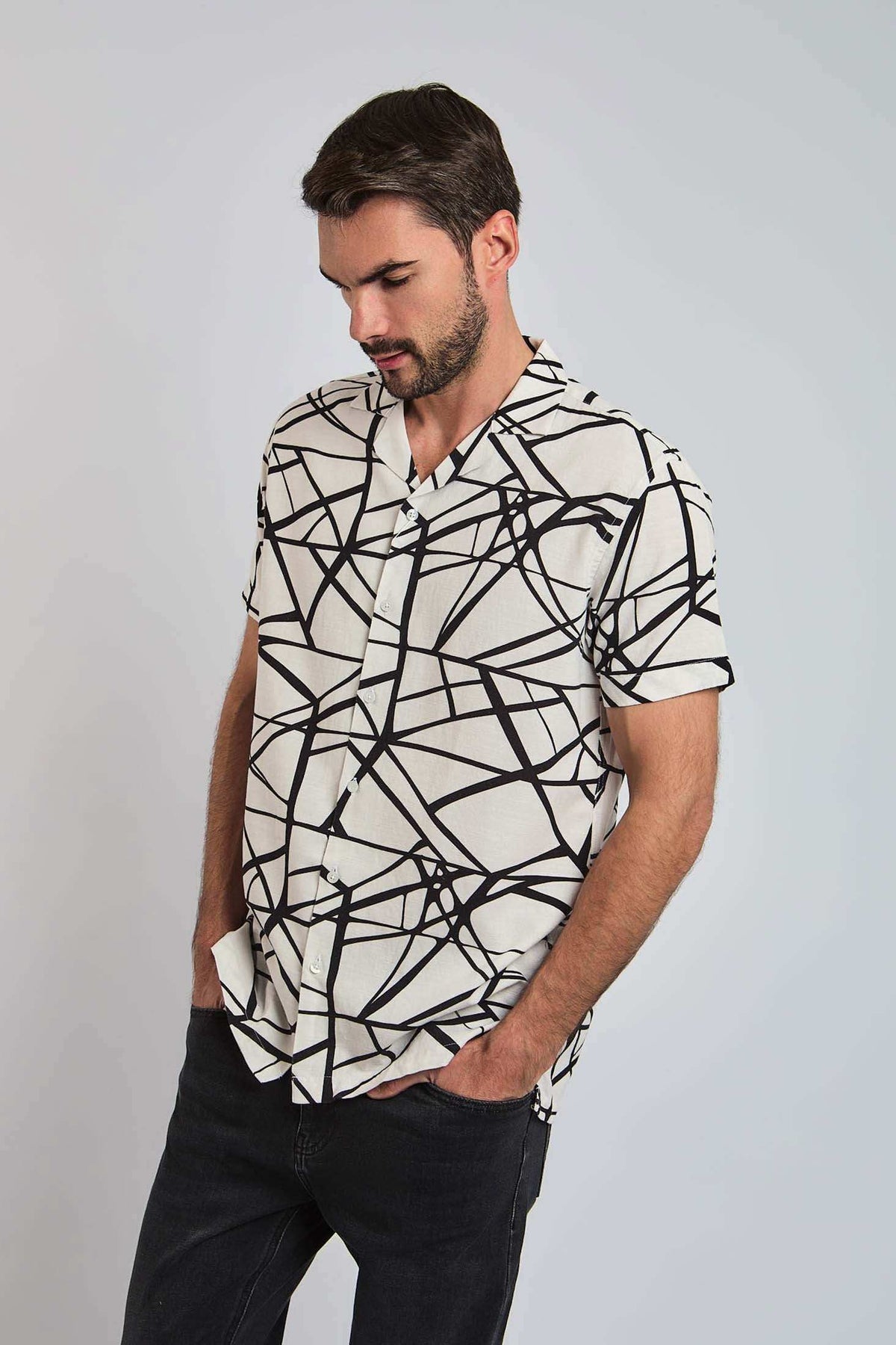 Man wearing short-sleeve black and white abstract print button-up shirt and dark jeans