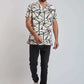 Man wearing short sleeve geometric print shirt, dark jeans, and white sneakers