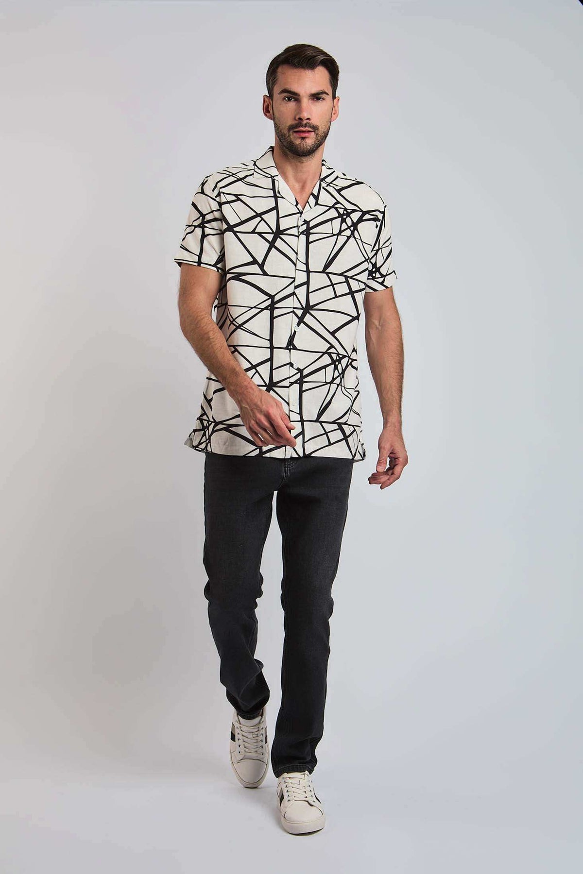 Man wearing short sleeve geometric print shirt, dark jeans, and white sneakers