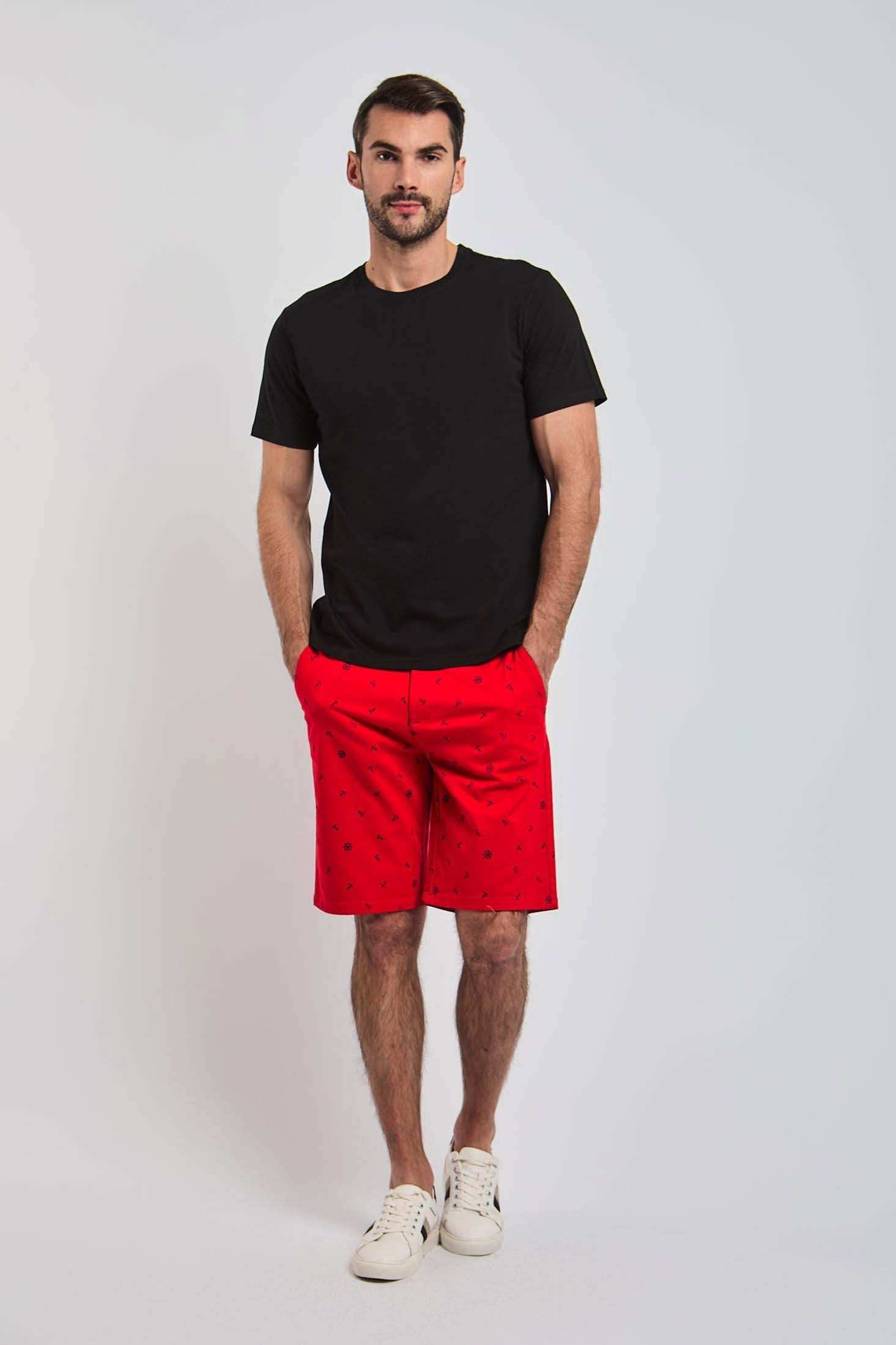 Man modeling Dalydress casual black t-shirt and red shorts with white sneakers on plain background