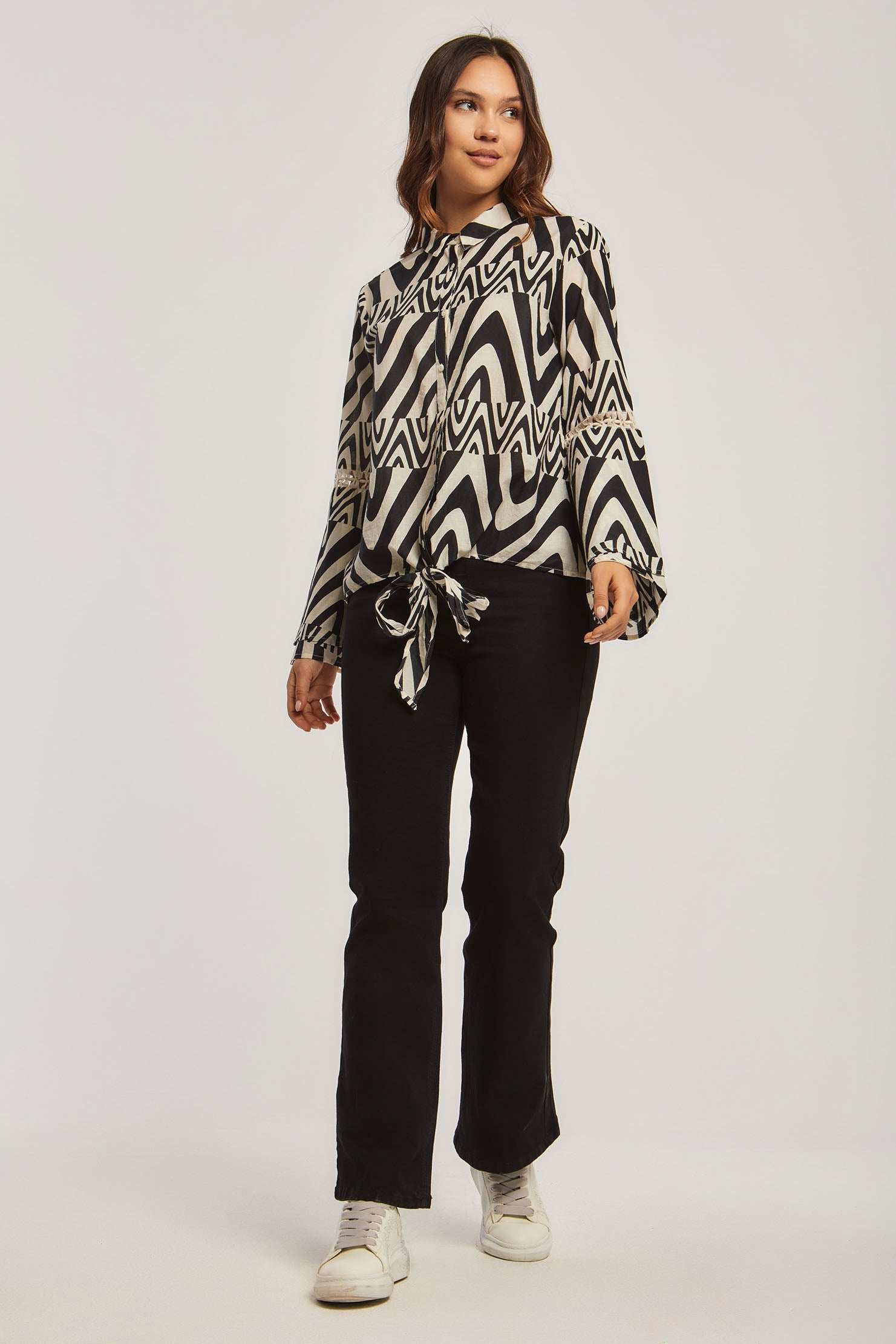 Woman in Dalydress black and white patterned blouse, black pants, and white sneakers