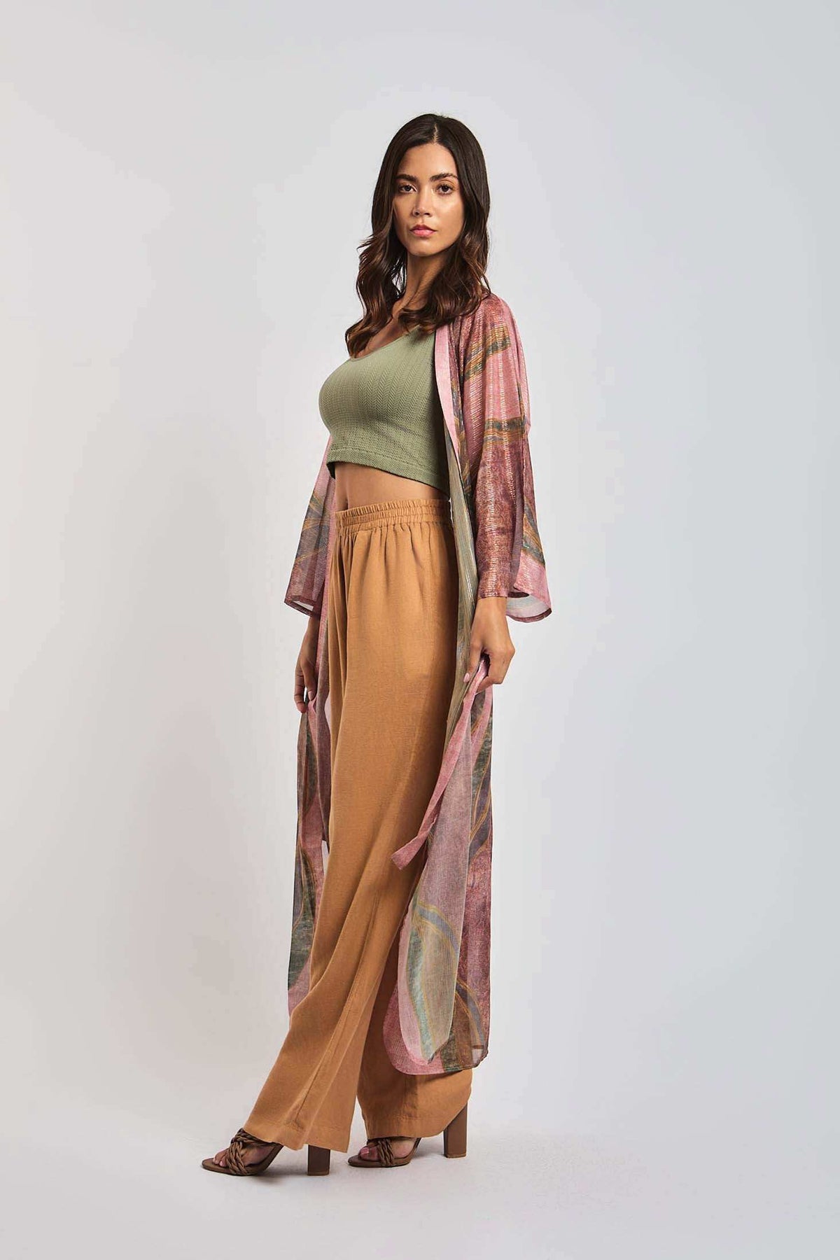 Woman in casual chic outfit with green crop top, tan high-waisted pants, and sheer pink kimono