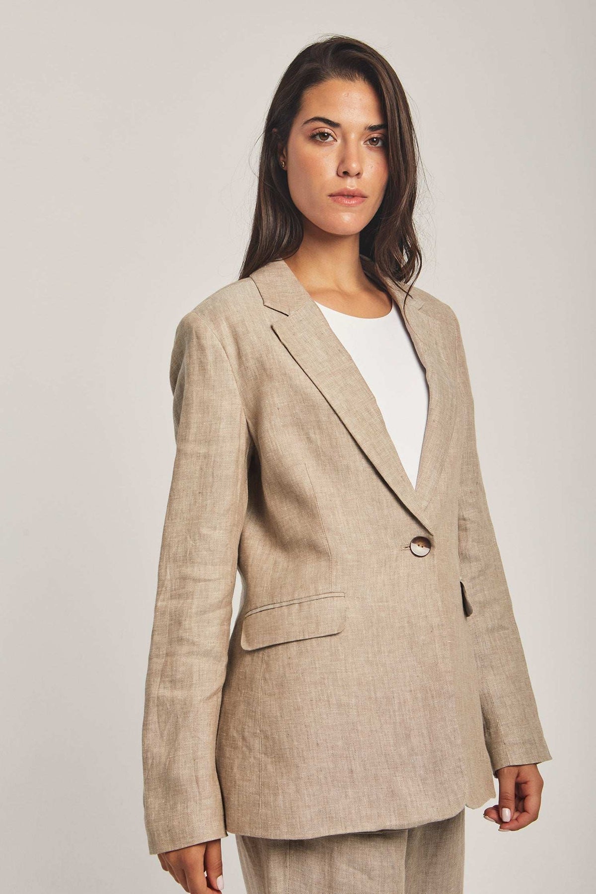 Woman wearing beige linen blazer and pants from Dalydress against plain background