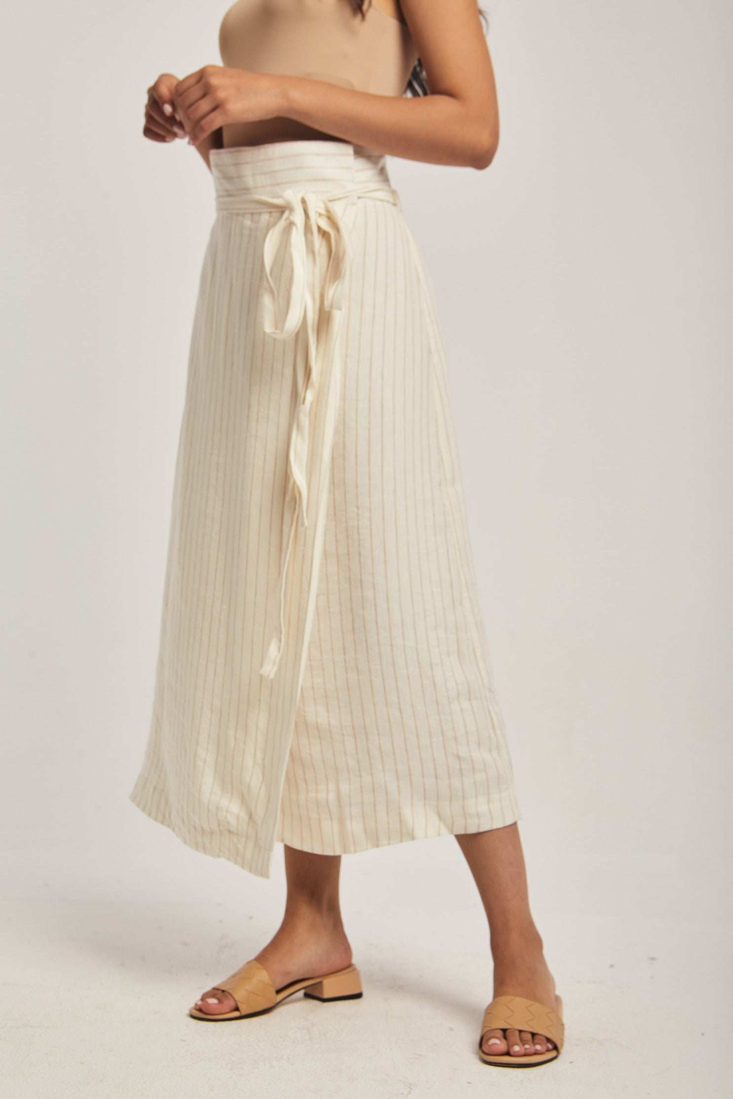 Woman wearing a cream striped midi skirt with tie waist from Dalydress, styled with sandals.