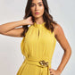 Woman wearing sleeveless yellow Dalydress dress with floral waist detail, posing against light background
