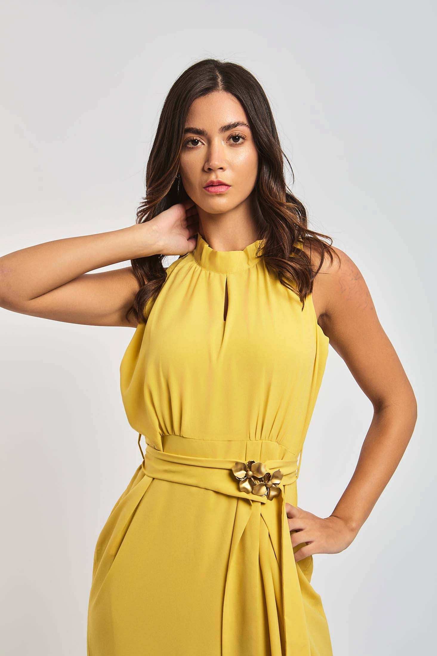 Woman wearing sleeveless yellow Dalydress dress with floral waist detail, posing against light background