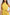 Woman wearing sleeveless yellow Dalydress dress with ruffled neck and gold floral belt accent
