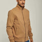 Man wearing tan zip-up jacket with stand collar and blue jeans on neutral background