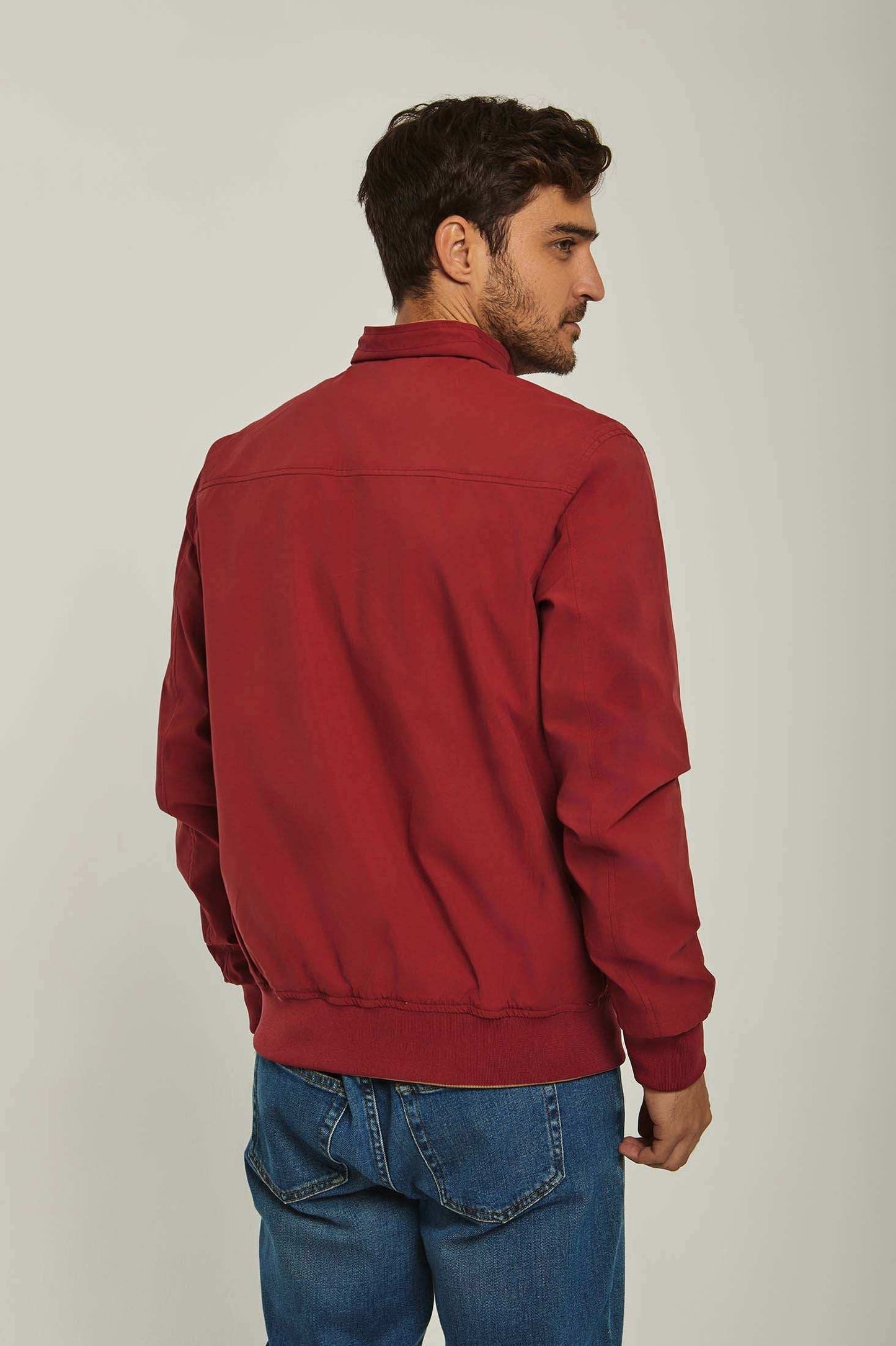 Man wearing a casual red jacket and blue jeans, back view, neutral background