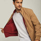 Man wearing tan jacket with red lining over white t-shirt and blue jeans, casual menswear