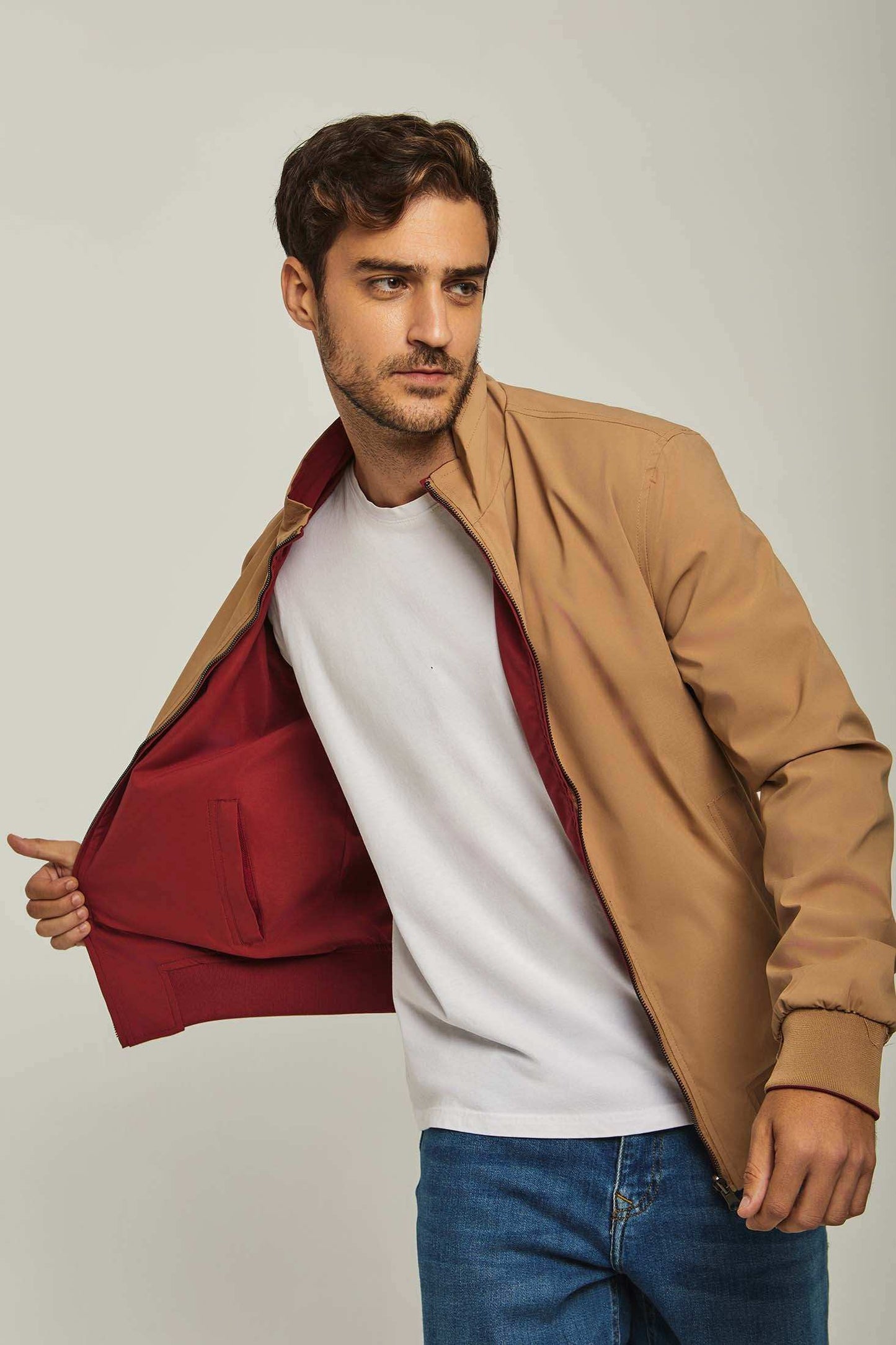 Man wearing tan jacket with red lining over white t-shirt and blue jeans, casual menswear