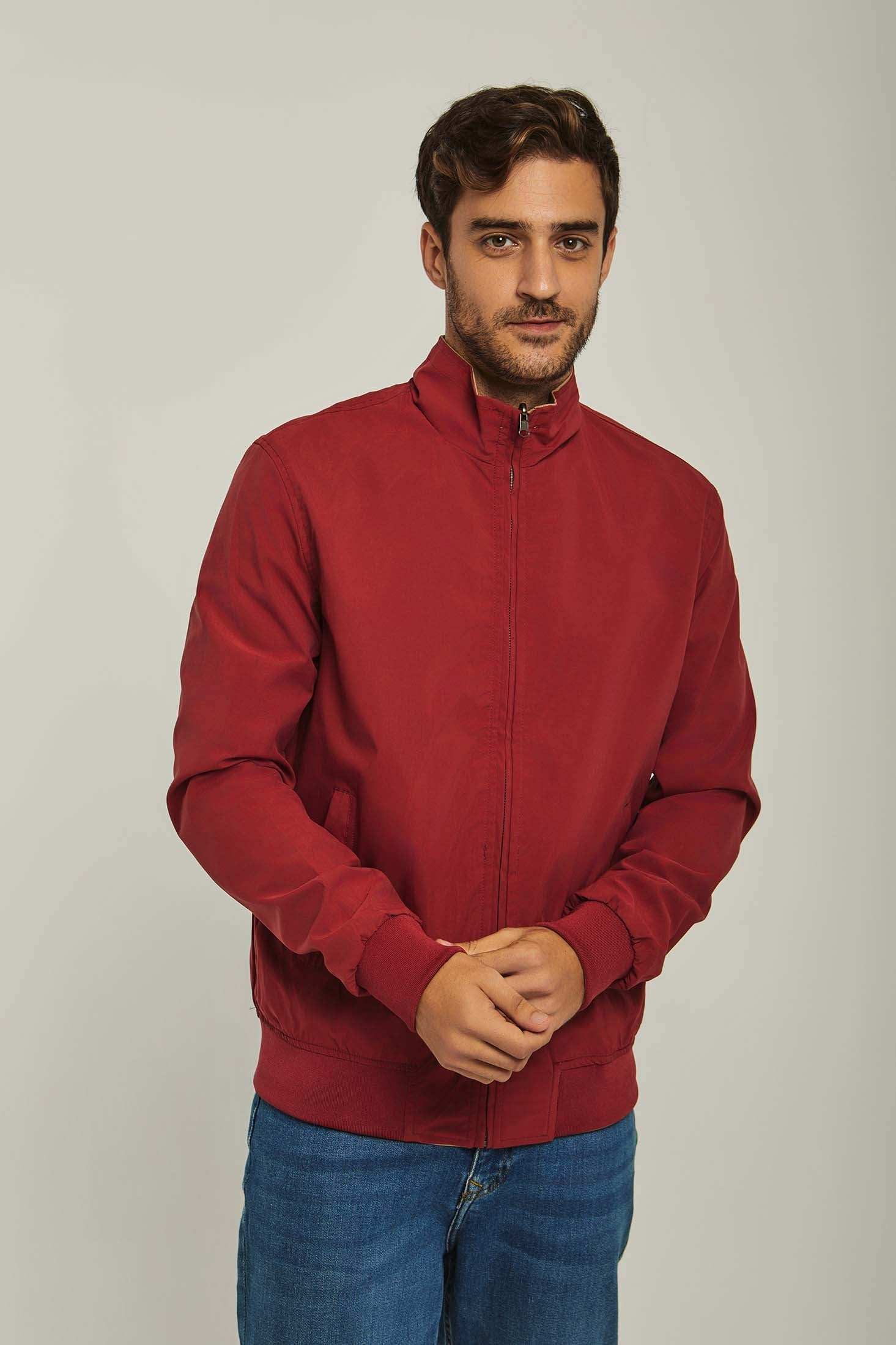 Man wearing a red zip-up casual jacket with blue jeans on a plain background