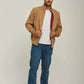 Man in casual tan jacket, white t-shirt, blue jeans, and white sneakers standing