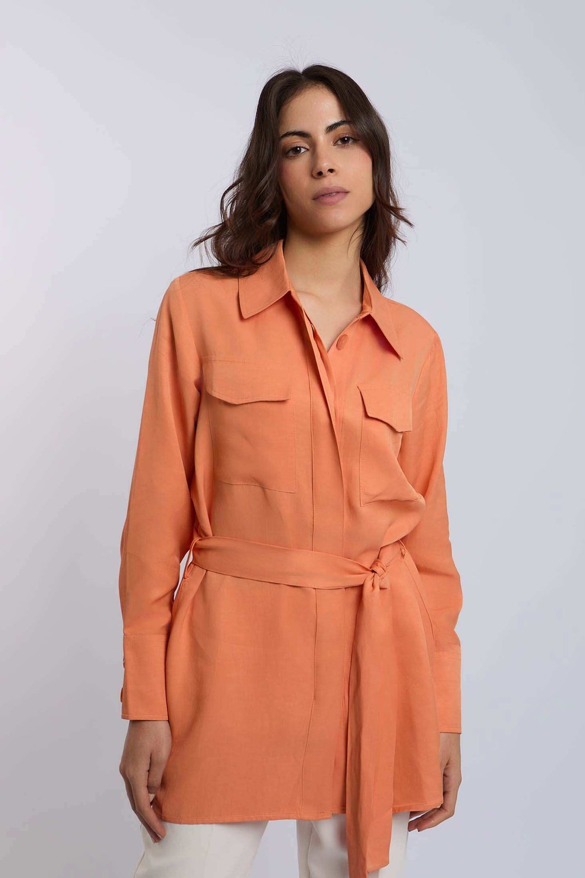 Woman wearing an orange belted long-sleeve Dalydress shirt with chest pockets.