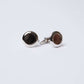 Round silver cufflinks with black and brown patterned inlays on white background