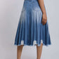 Woman wearing pleated denim midi skirt with frayed hem and white sneakers, back view