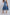 Woman wearing pleated denim midi skirt with frayed hem and white sneakers, back view