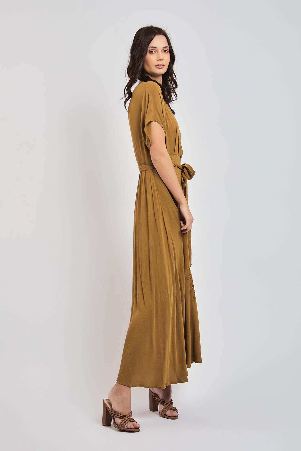 Woman in mustard yellow maxi dress with short sleeves and waist tie, side view