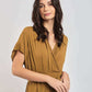 Woman wearing a mustard yellow wrap dress with short sleeves and lace trim, posing indoors
