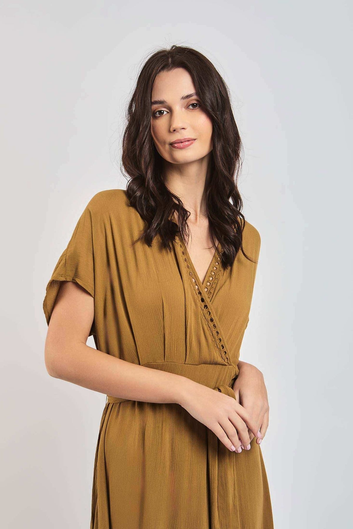 Woman wearing a mustard yellow wrap dress with short sleeves and lace trim, posing indoors