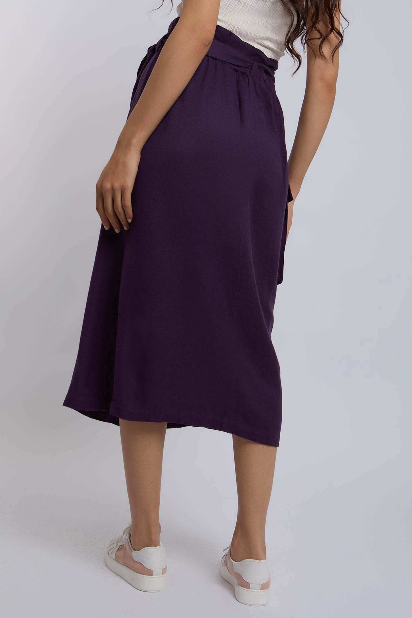 Woman wearing a high-waisted purple midi skirt with white sneakers, back view