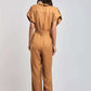 Woman wearing a short-sleeve camel jumpsuit, viewed from the back, with block heel shoes