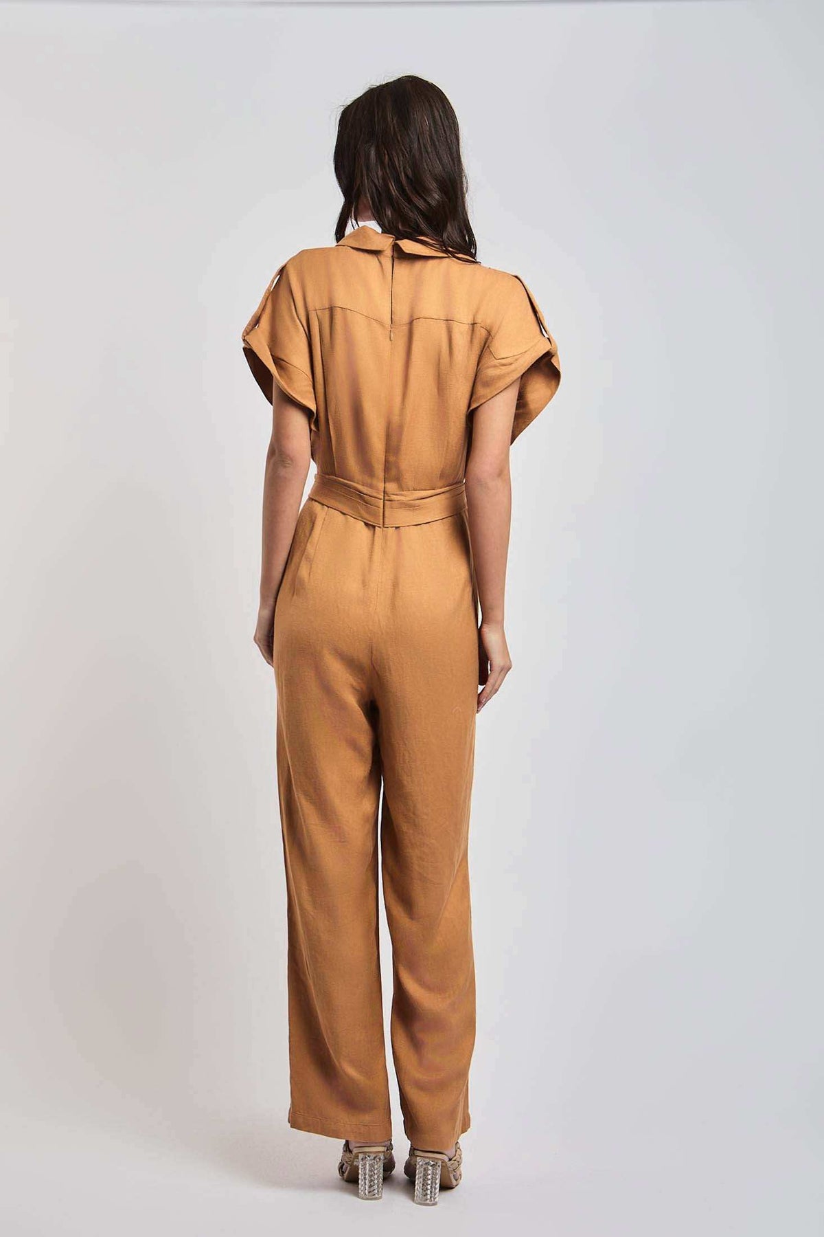 Woman wearing a short-sleeve camel jumpsuit, viewed from the back, with block heel shoes