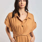 Woman in tan belted short sleeve shirt dress with collar, hands in pockets, neutral background