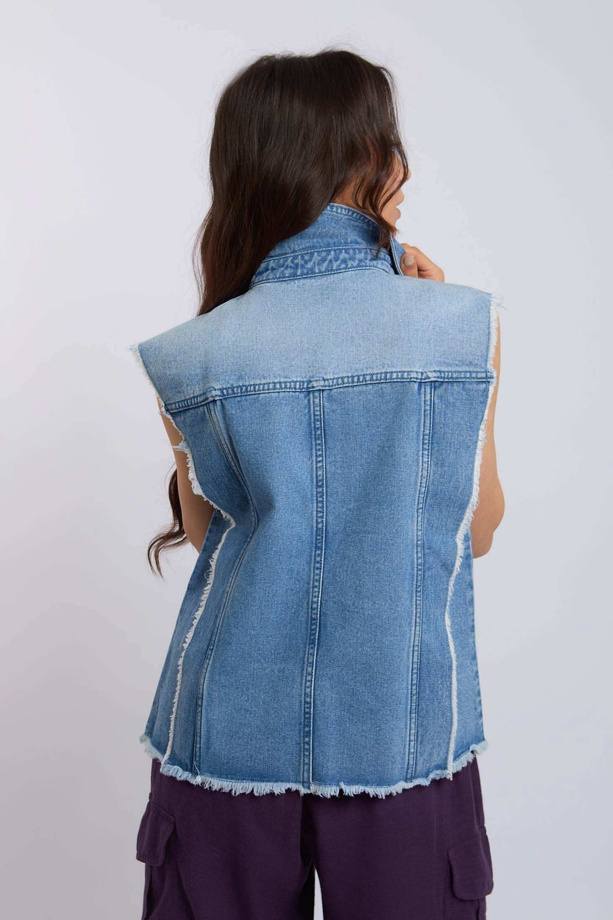Woman wearing sleeveless denim vest with frayed edges, shown from the back