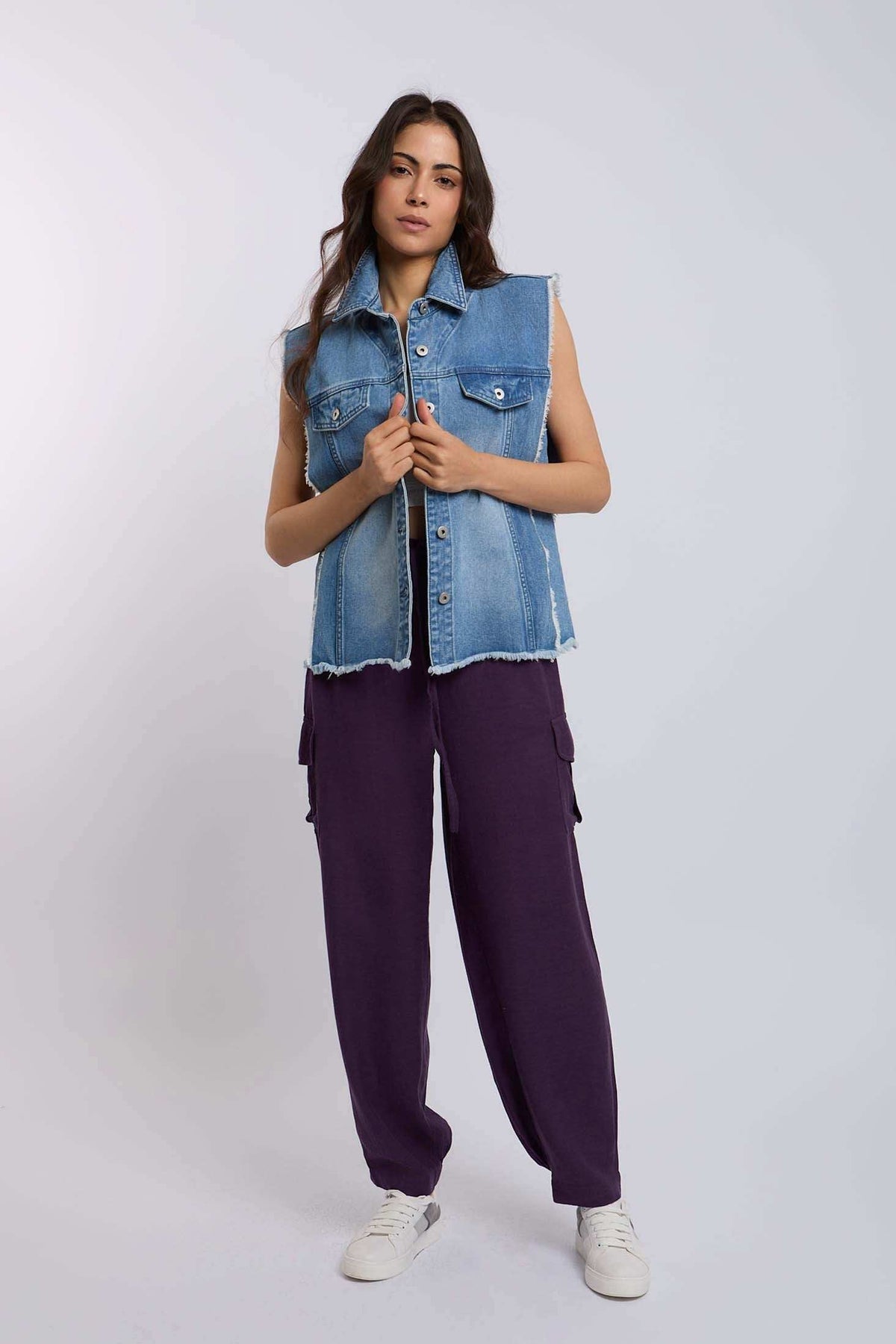 Woman wearing sleeveless denim vest and purple cargo pants with white sneakers