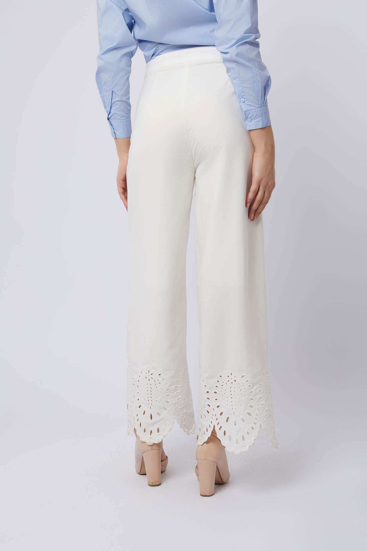 Woman wearing wide-leg white pants with eyelet lace hem and blue button-up shirt