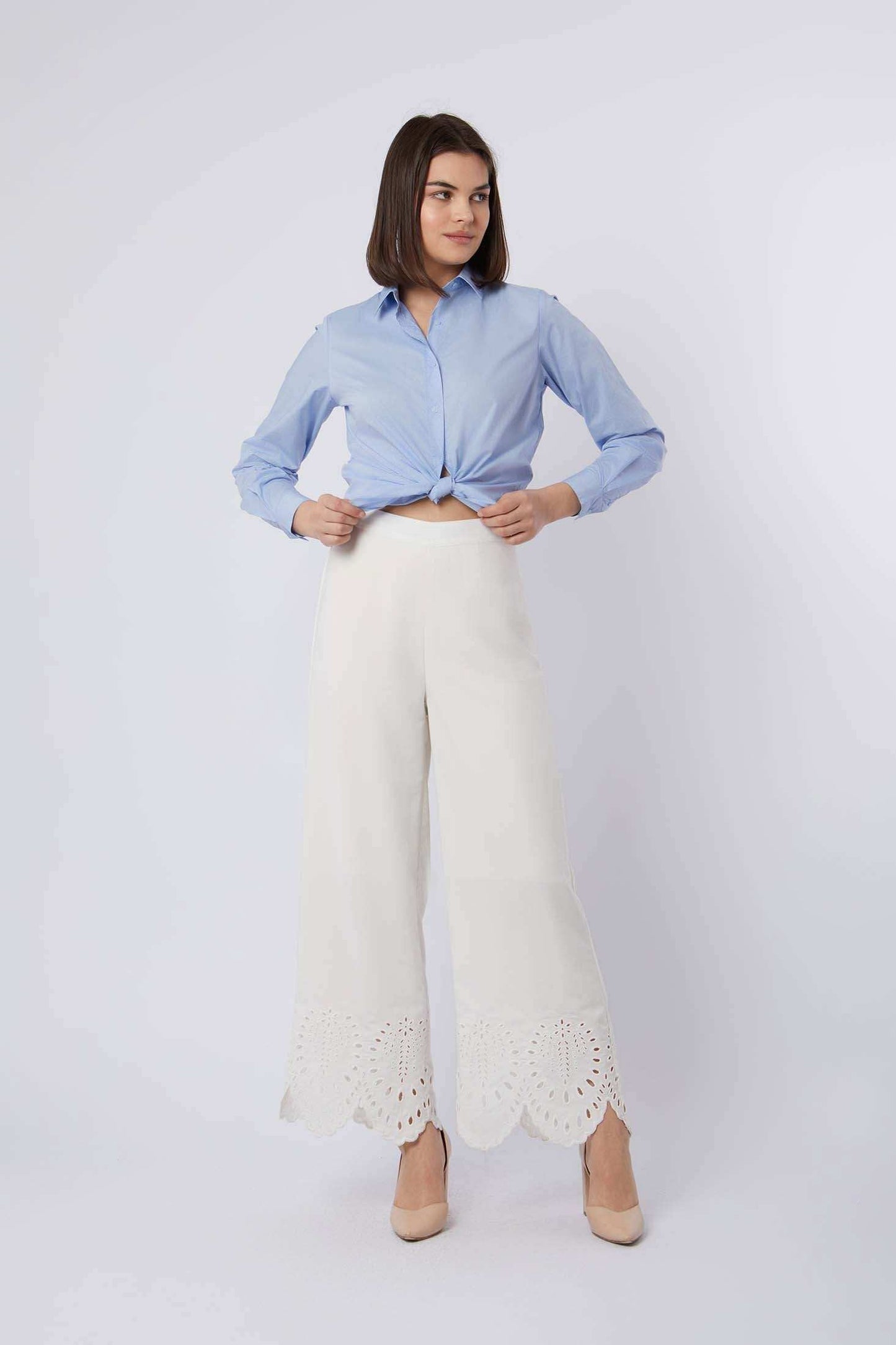 Woman wearing a light blue button-up shirt and white wide-leg pants with lace hem