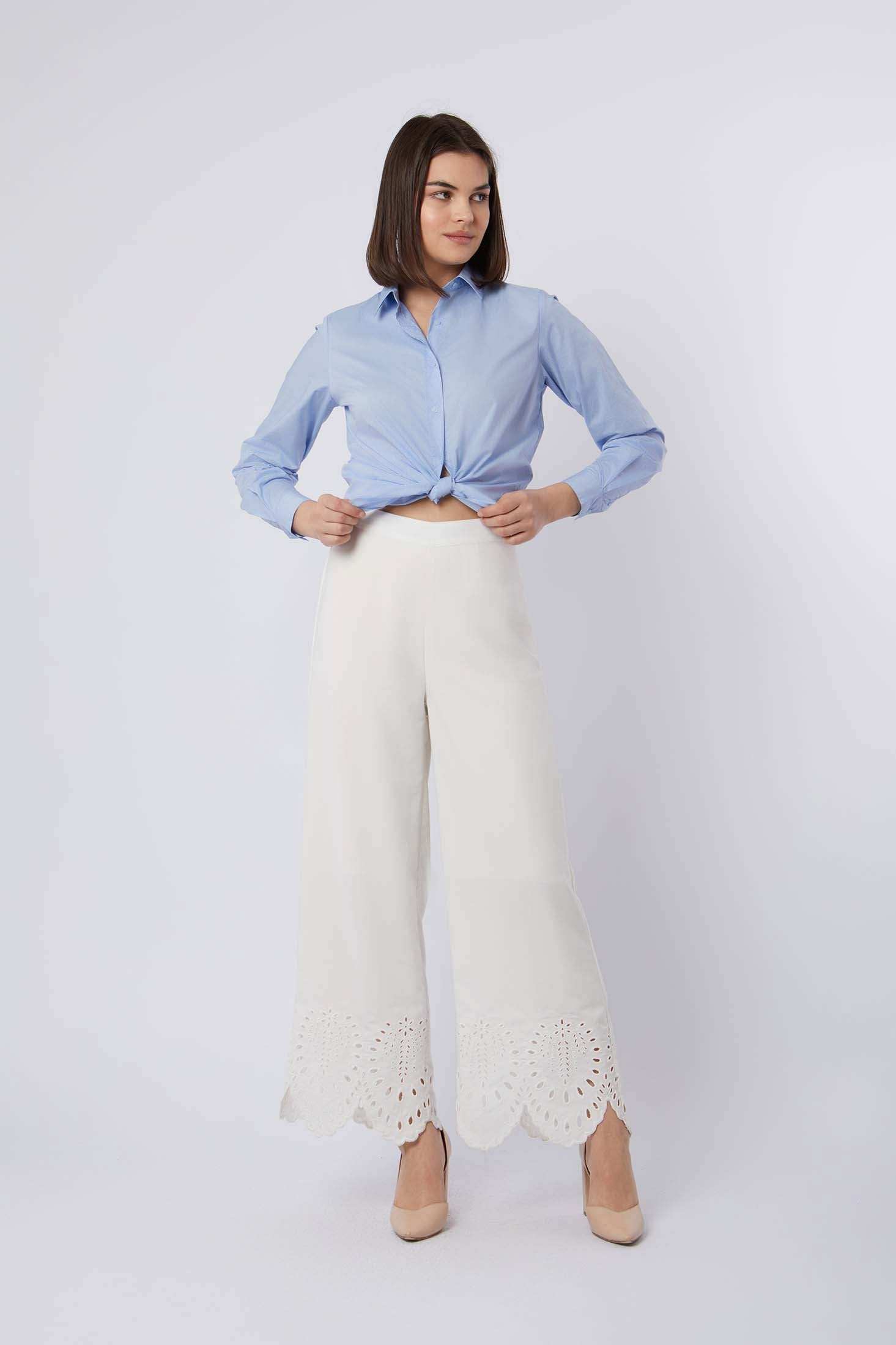 Woman wearing a light blue button-up shirt and white wide-leg pants with lace hem