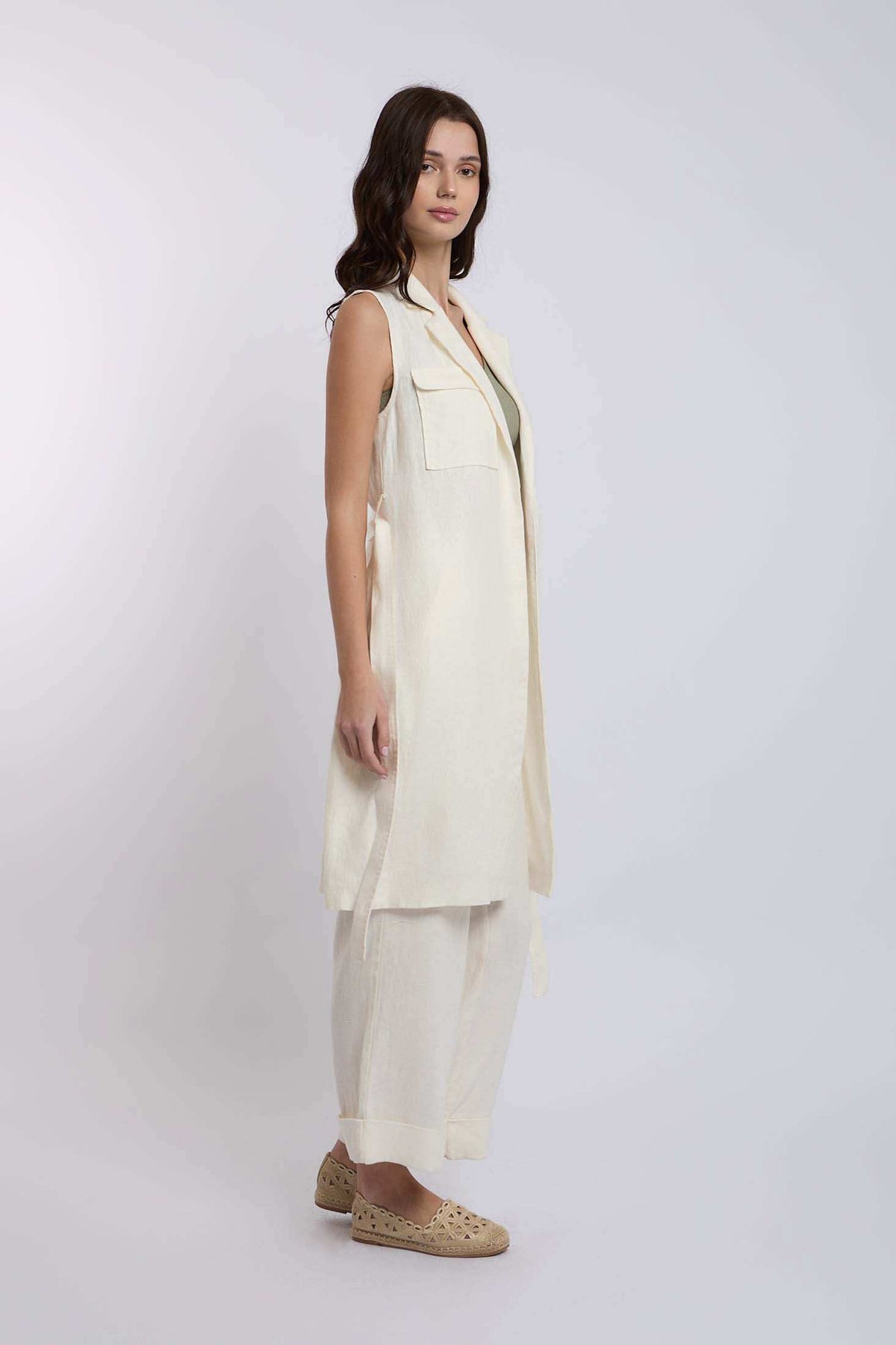 Woman wearing sleeveless cream long vest, matching wide-leg pants, and woven flats