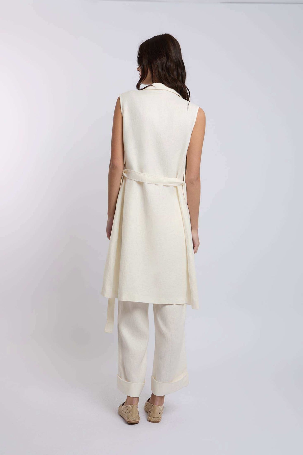 Woman wearing sleeveless cream belted tunic and wide-leg pants set, rear view