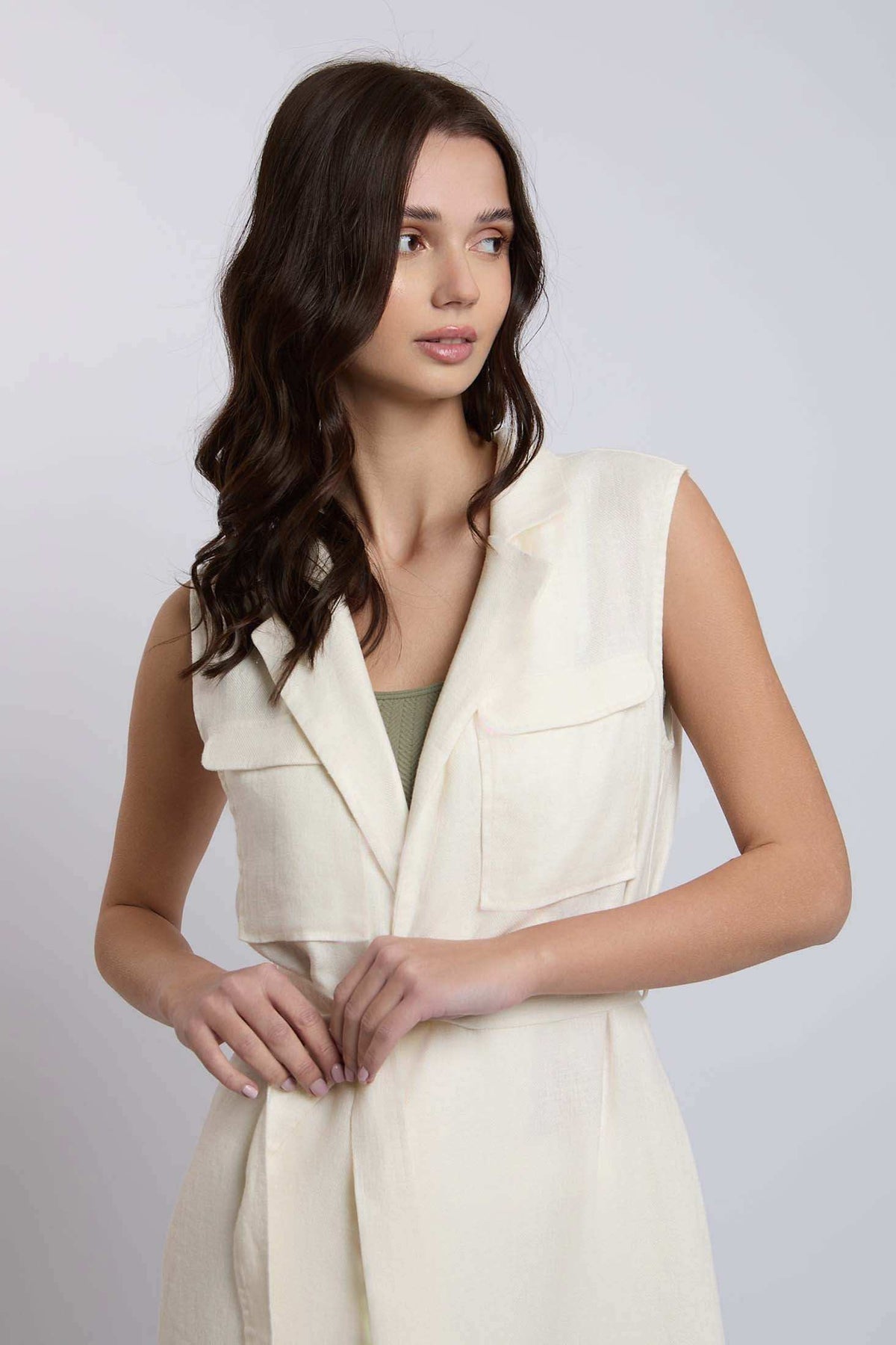 Woman wearing sleeveless cream belted vest with flap pockets, casual urban style
