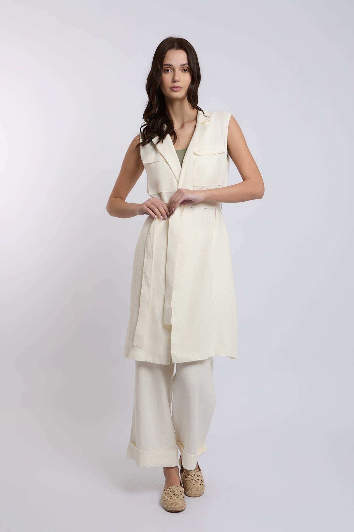 Woman wearing sleeveless beige long vest with matching wide-leg pants and woven slip-ons