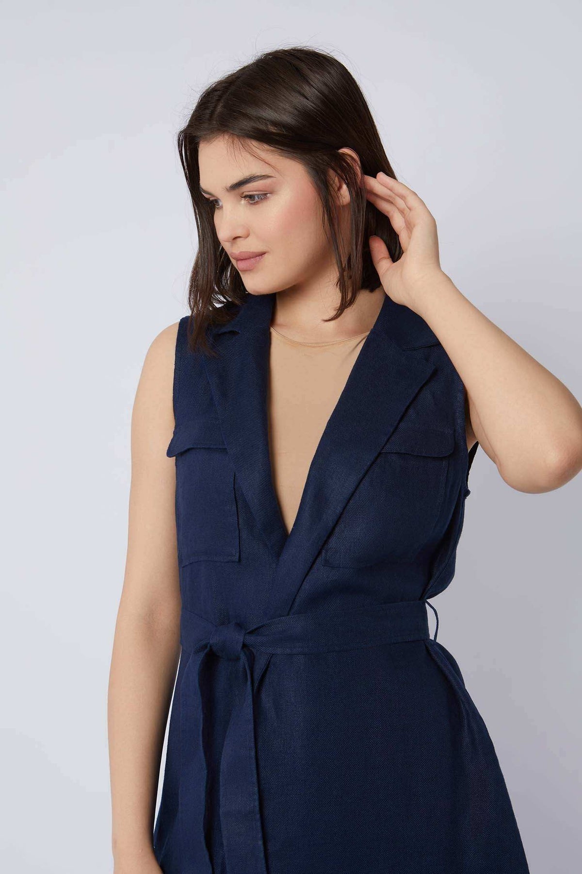 Woman wearing sleeveless navy blue belted vest with deep V-neck and flap pockets