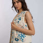 Woman wearing sleeveless cream vest with blue floral embroidery and beige pants