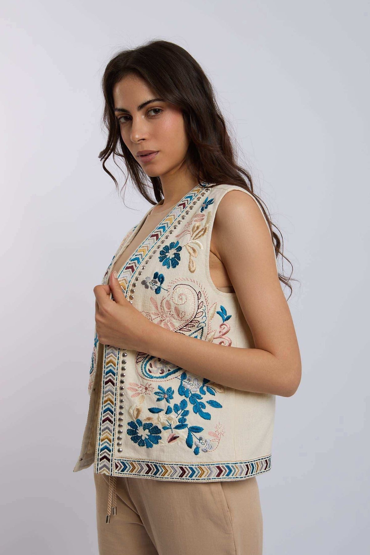 Woman wearing sleeveless cream vest with blue floral embroidery and beige pants