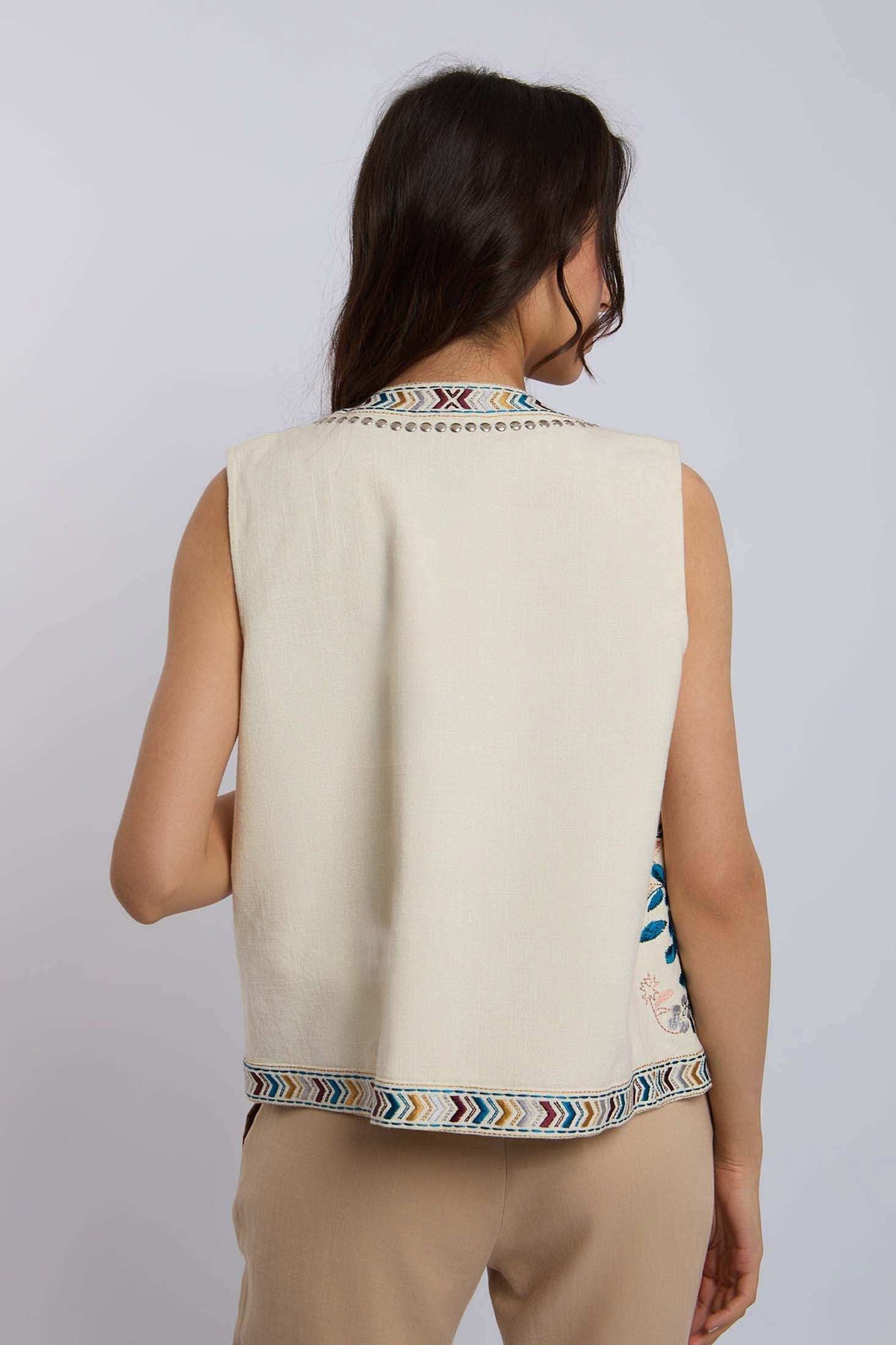 Woman wearing a sleeveless cream vest with colorful embroidered trim, viewed from the back